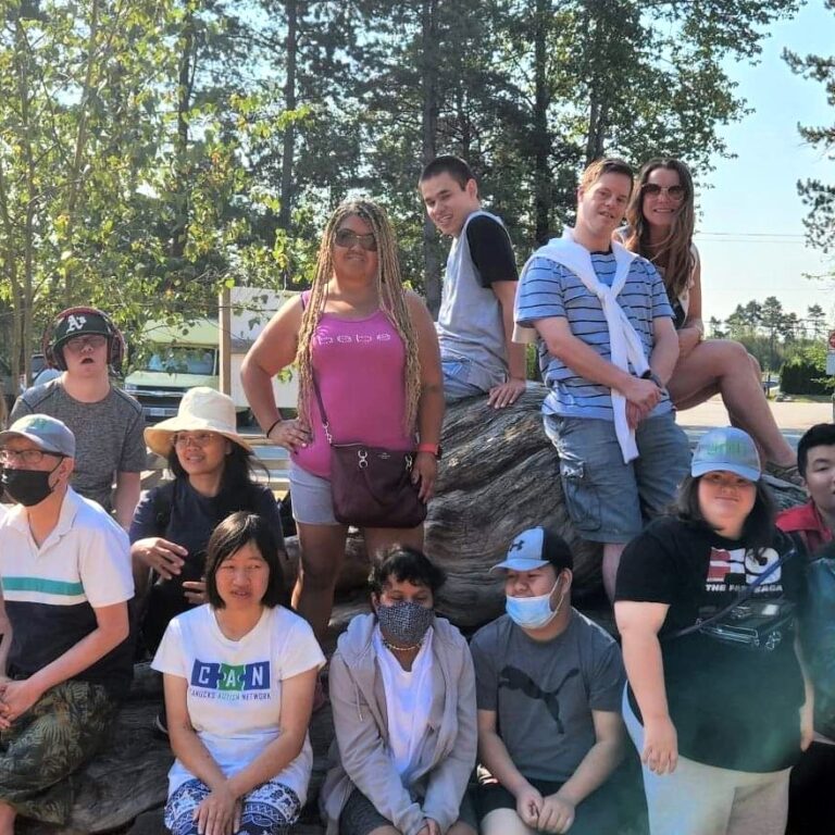 People in UNITI's Day Services pose for a picture outside by a giant log in summer.