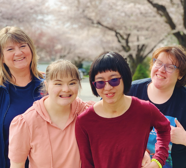 4 members of the UNITI community smile for a photo outside in front of cherry blossom trees.