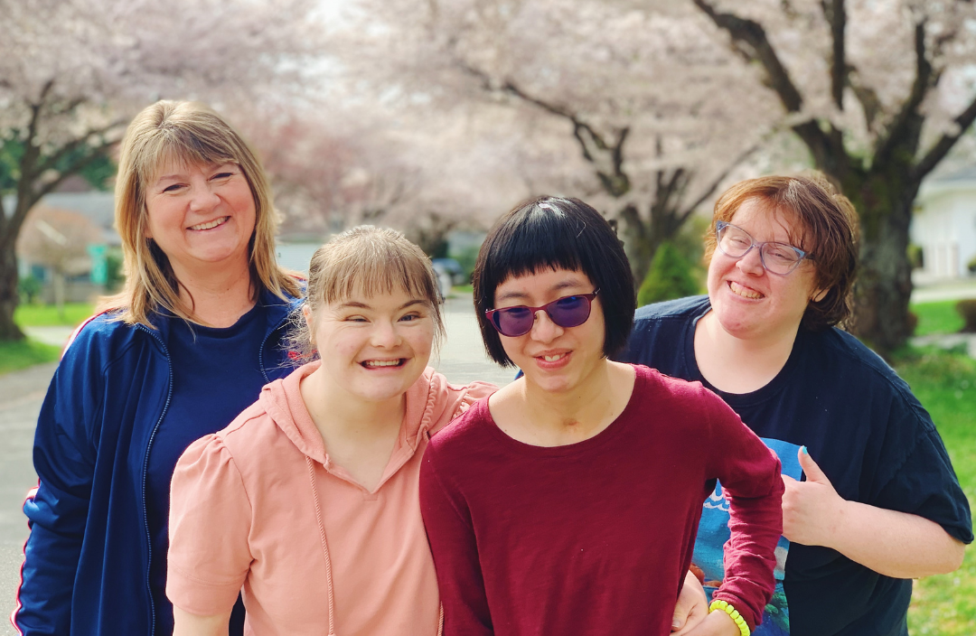 4 members of the UNITI community smile for a photo outside in front of cherry blossom trees.